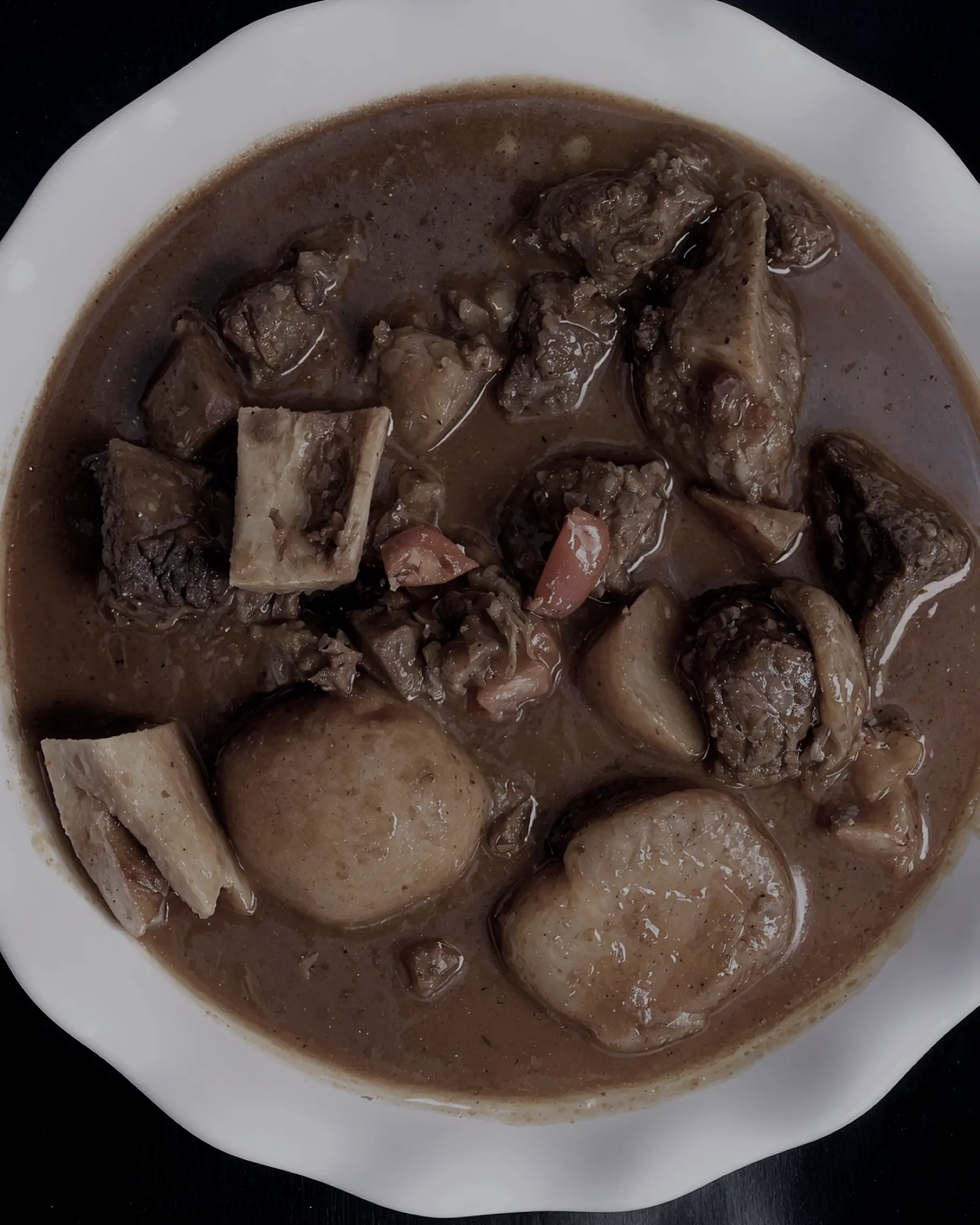 Goat curry in a white bowl, shot from above on black.