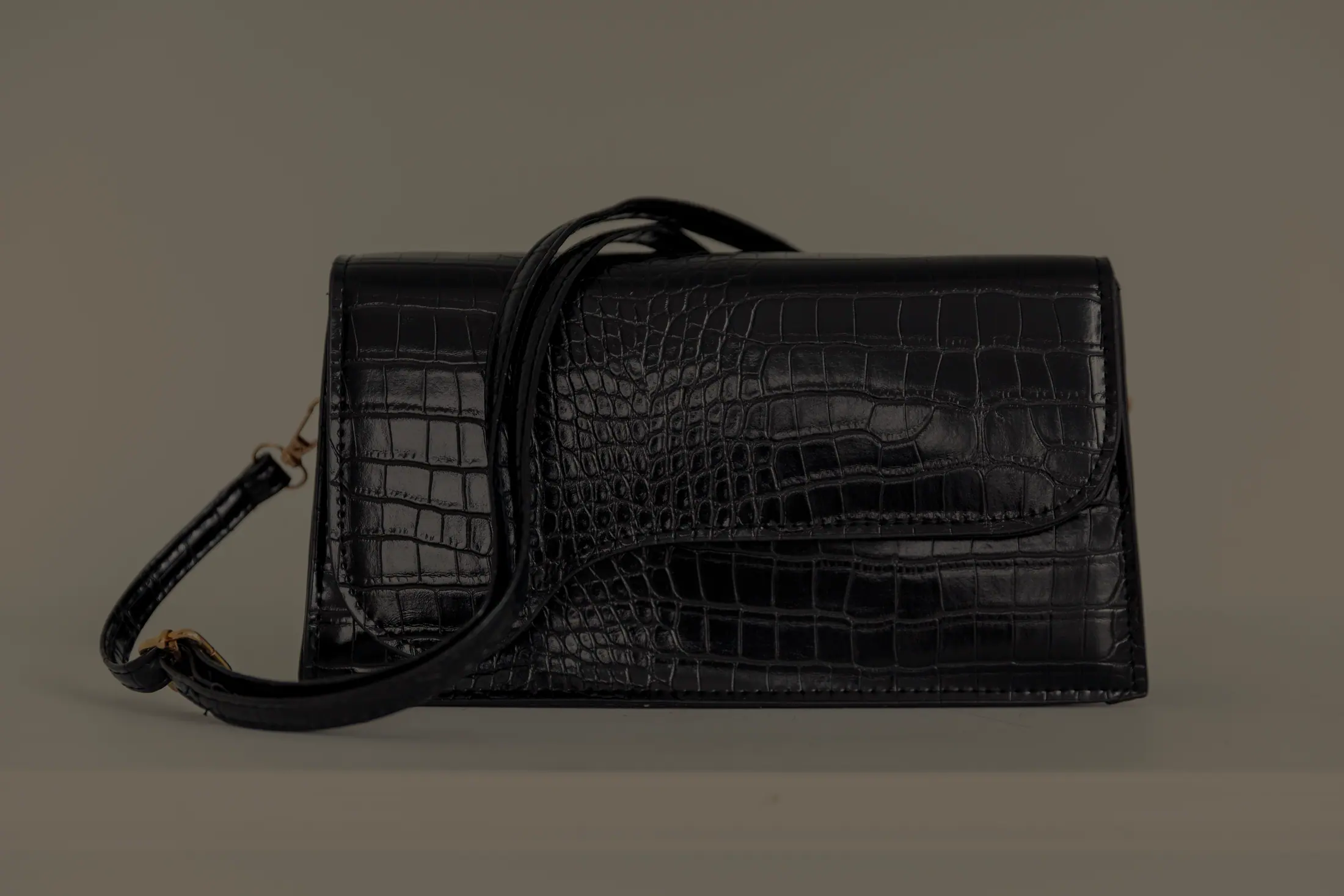 A black patent shoulder bag on a grey seamless.