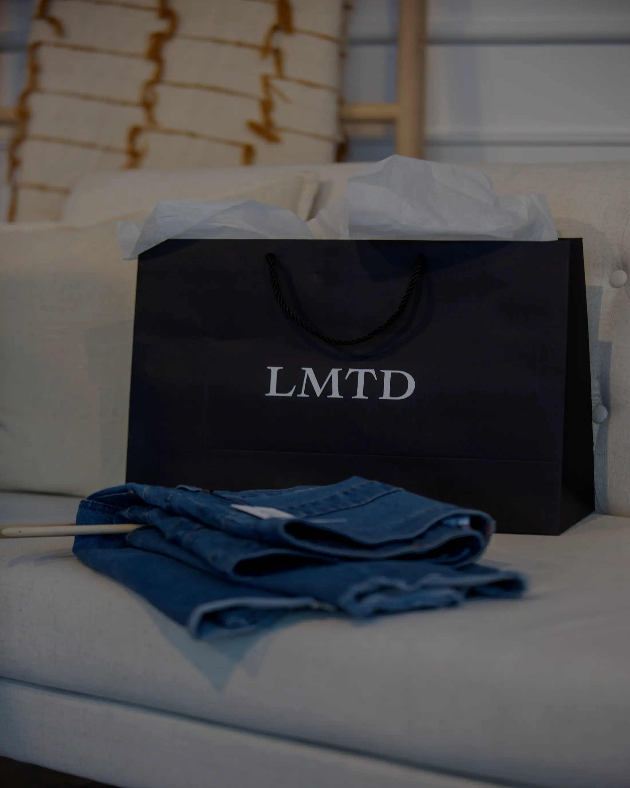 A branded shopping bag and folded denim on a sofa.