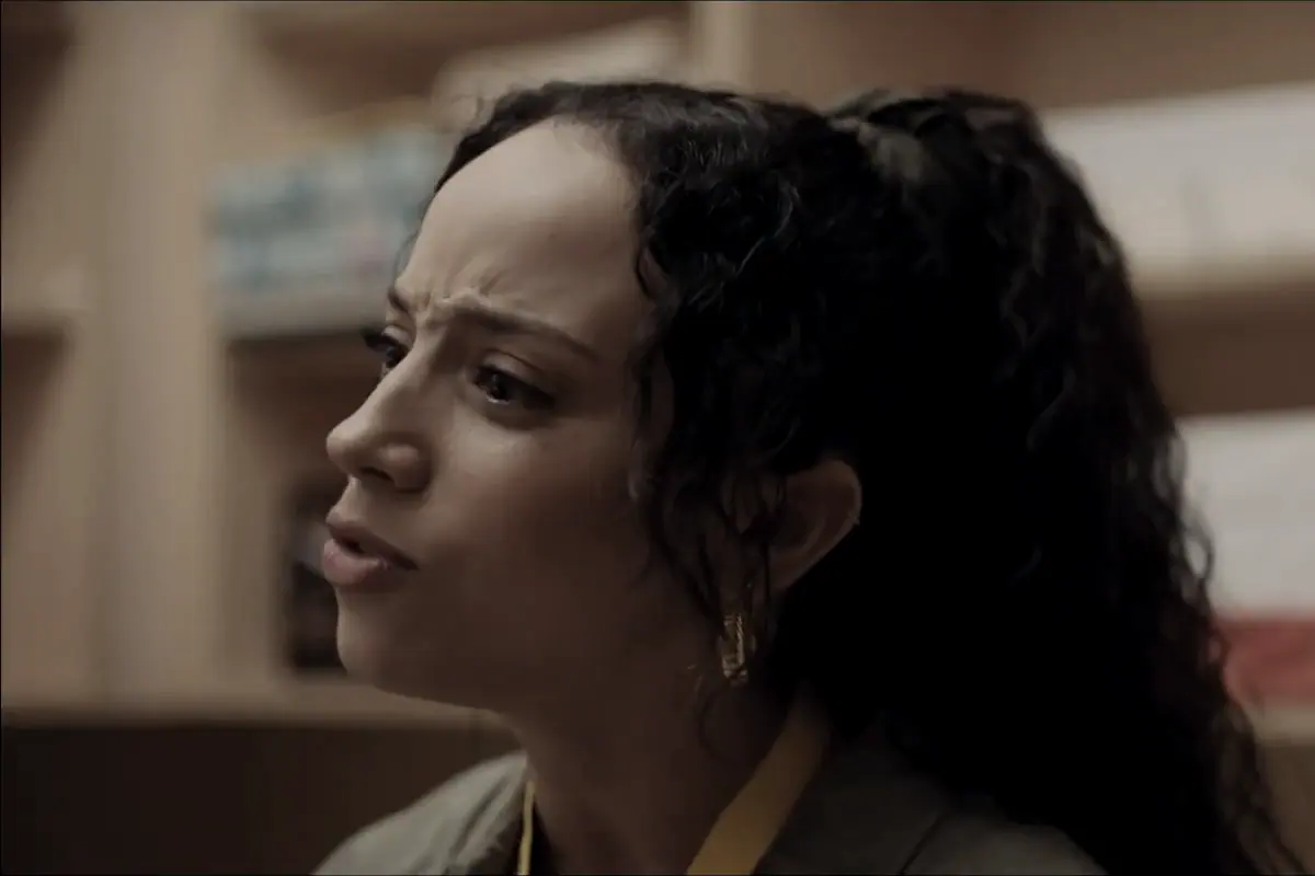 A woman in a school office, mid sentence, shelves of files behind her.