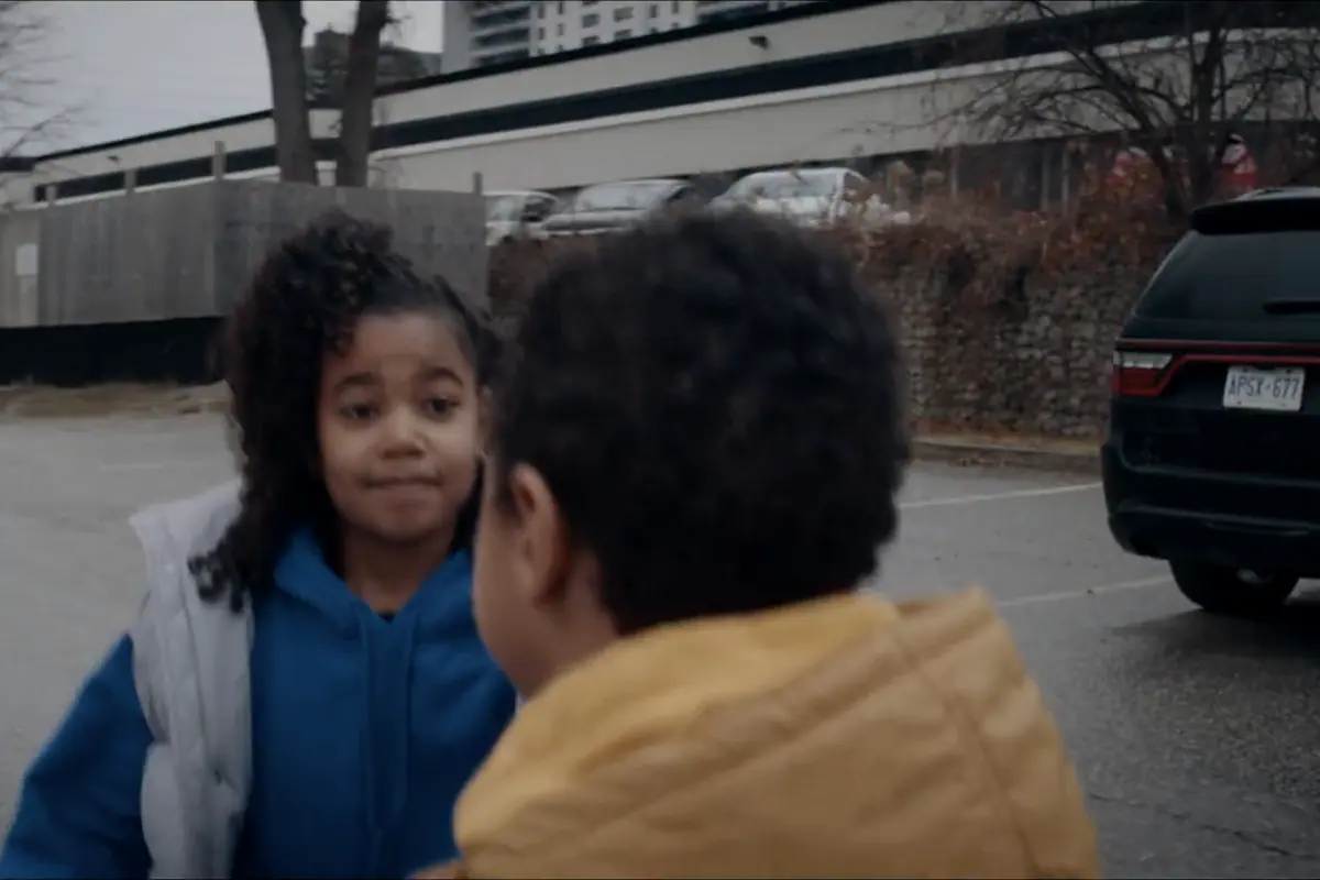 Two children talking on a suburban street beside a parked car.
