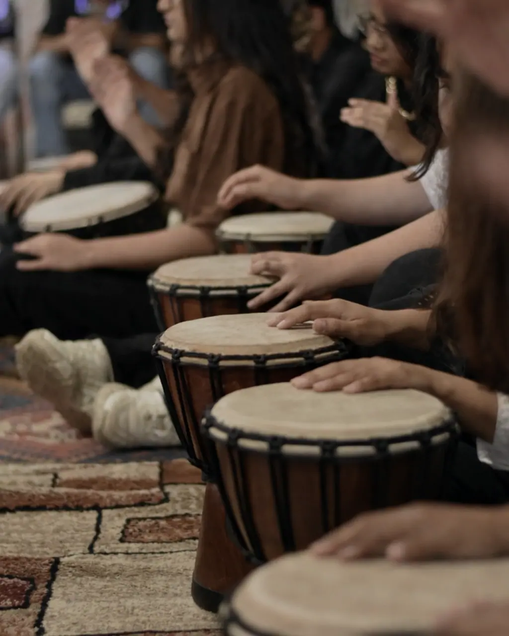 A row of hands playing hand drums in a circle.
