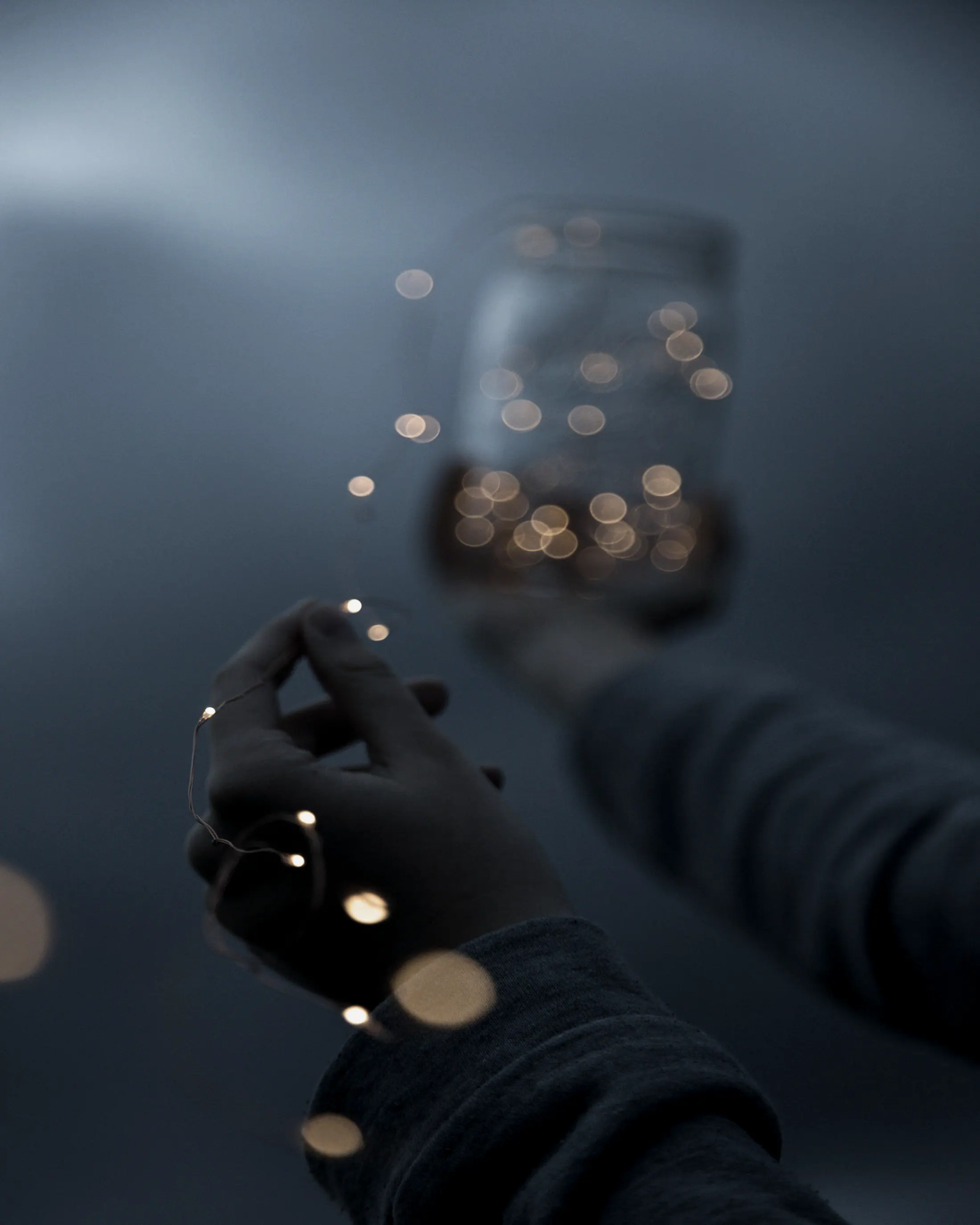 A hand holding a jar of warm fairy lights against deep blue.